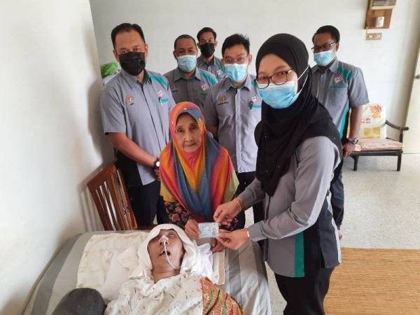 Juzilawati (kanan) menyerahkan Mykad kepada Zainun bagi mewakili Azman ketika program penyerahan kad pengenalan di rumahnya di Lorong 12, Kubang Buaya pada Rabu.