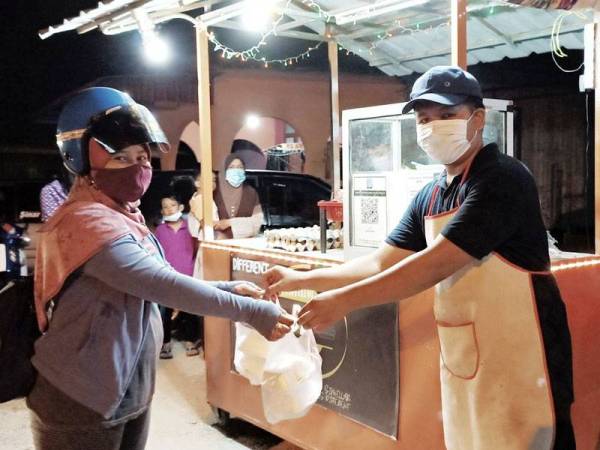 Wan Muhammad Iqbal mengagihkan burger percuma kepada orang ramai yang datang ke gerainya di Selising, Pasir Puteh sempena Hari Pembantu Perubatan.