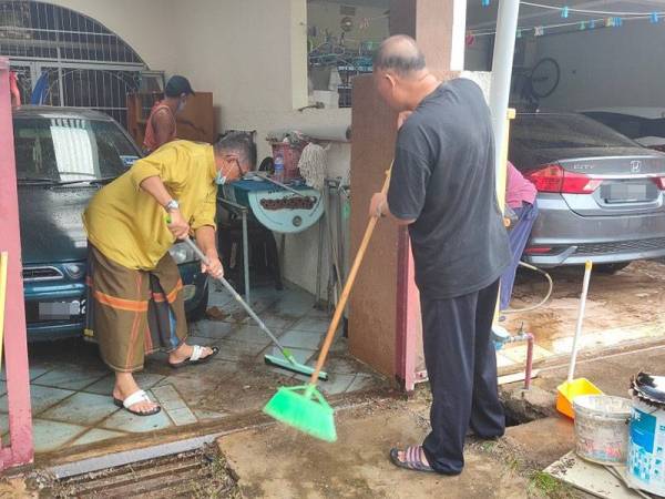 Hanafiah (kiri) sempat membantu penduduk membersihkan rumah yang dimasuki air ketika meninjau runtuhan itu di Taman Bukit Mentok, Kampung Pengkalan Pandan, Chukai, Kemaman pagi Jumaat.