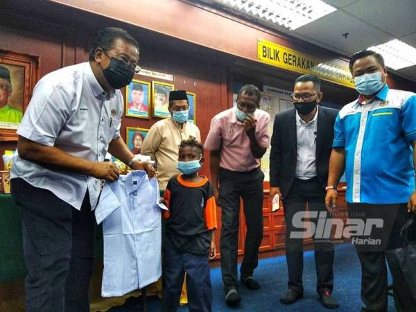 Abdul Rahman (kiri) menyarungkan uniform sekolah kepada penerima dari SK LKTP Kechau 1 sambil diperhatikan Pengarah Jakoa Pahang, Johari Alwi (kanan).