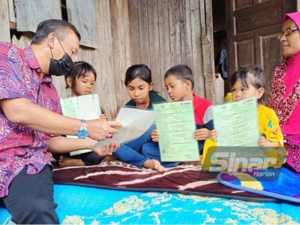 Ruslin (kiri) menyerahkan dokumen sijil kelahiran kepada empat beradik di Kampung Petai Dusun, Rantau Panjang menerusi Program Menyemai Kasih Rakyat (Mekar).