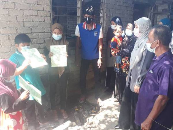 Madihah (dua dari kanan) turun menyerahkan sijil kelahiran kepada tiga beradik di Kampung Alor Serdang, Kota Sarang Semut, Alor Setar pada Ahad.