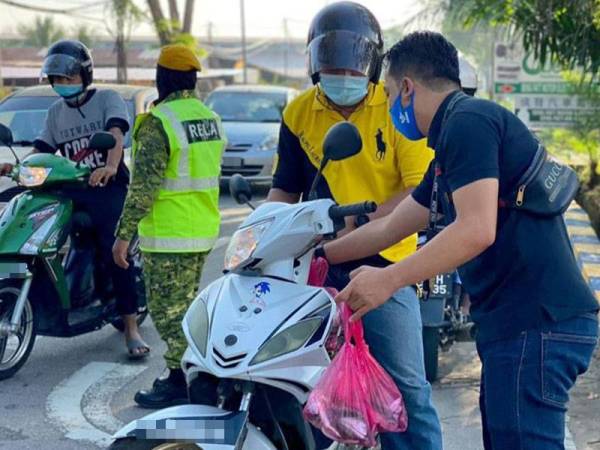 Baitul Mustawa (kanan) mengagihkan ikan kembung percuma secara pandu lalu kepada penduduk sekitar di Pusat Perniagaan Batu 40 di sini.
