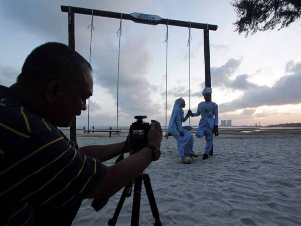 Jurugambar bebas, Mohd Rafiee Mohd Yusof (kiri) merakam gambar pasangan pengantin di Pantai Teluk Sisek hari ini. 