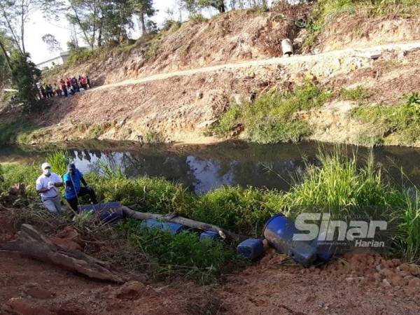 Hasni (kiri) melihat tong dan kesan hasil buangan di Sungai Kim Kim, Pasir Gudang pada Sabtu.