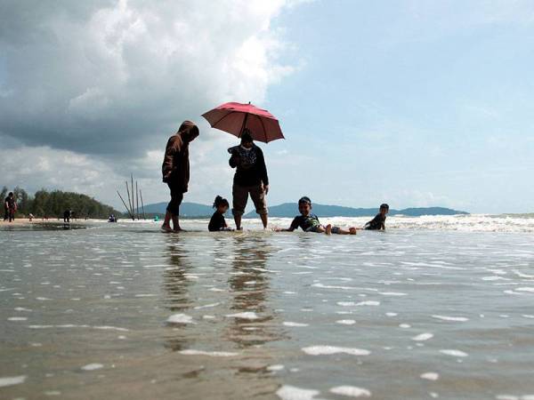 Sharifah Rokiah Syed Hamid, 60, (berdiri,kanan) berpayung berikutan cuaca panas semasa menemani cucunya mandi-manda di Pantai Kempadang hari ini.