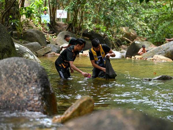 Pengunjung, Mohamad Shahmirul Aswad Sabaruddin, 24, (kanan) bersama adiknya Muhammad Dahmin Izmar Aqif Sabaruddin, 18, (kiri) mengutip sampah sarap yang hanyut di air terjun sempena Hari Air Sedunia, di Air Terjun Taman Eko Rimba Kledang Saiong hari ini.  