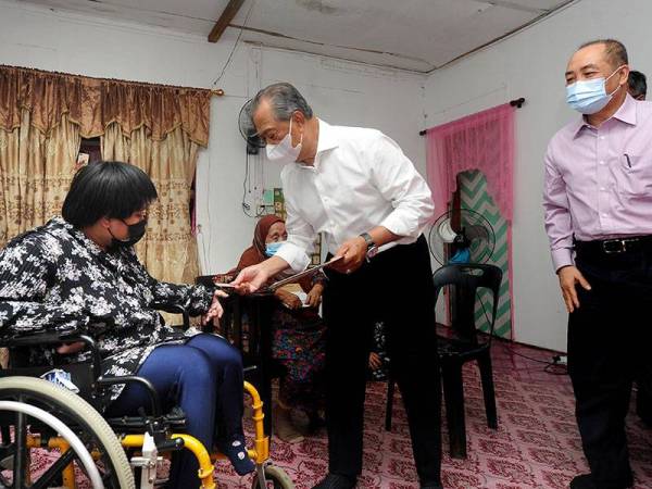 Perdana Menteri Tan Sri Muhyiddin Yassin (dua, kanan) menyerahkan kad Orang Kurang Upaya (OKU) dan bantuan kepada penerima bantuan, Nur Elfi Hanum Ismail, 27, (kiri) sewaktu mengadakan ziarah prihatin di Kampung Sembulan Tengah, hari ini. 