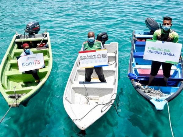 Sebahagian penggiat sektor pelancongan memegang plakad tanda sokongan terhadap program Komunikasi Tindakan Setempat (KomTiS): Pembudayaan Norma Baharu di Pulau Perhentian, pada Ahad.