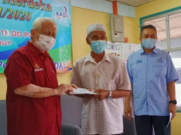 Kamarudin (kiri) menyampaikan sumbangan pada Majlis Pembahagian Hasil Ladang Merdeka Meranti, Senor dan Bakong Bagi Musim 1/2020 di Pertubuhan Peladang Kawasan (PPK) Kubang Bunut, Pasir Mas.