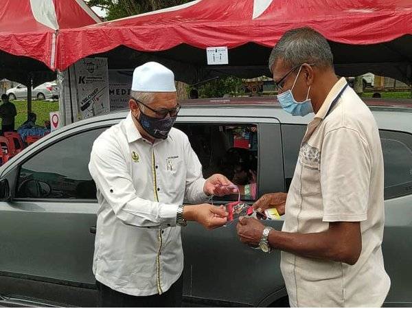 Razman (kiri) menyerahkan kolar tanda pengenalan vaksinasi dan risalah kepada seorang pemilik anjing, P Nagasegaran ketika Program Pemvaksinan Anti Rabies 2021 Daerah Larut Matang dan Selama di depan pasar raya The Store Kamunting, di sini pada Ahad.