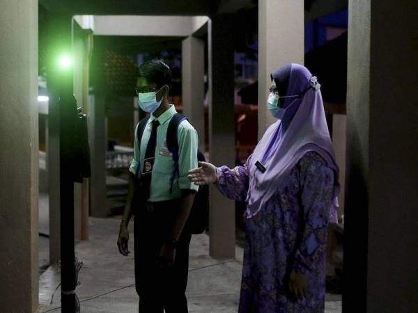 Guru Pengajian Am Zahrah Ahmad memantau pelajarnya untuk mengimbas suhu badan sebelum dibenarkan memasuki perkarangan sekolah bagi memulakan sesi persekolahan hari pertama bagi peringkat menengah di Sekolah Menengah Kebangsaan (SMK) Forest Height,Negeri Sembilan hari ini. - Foto Bernama