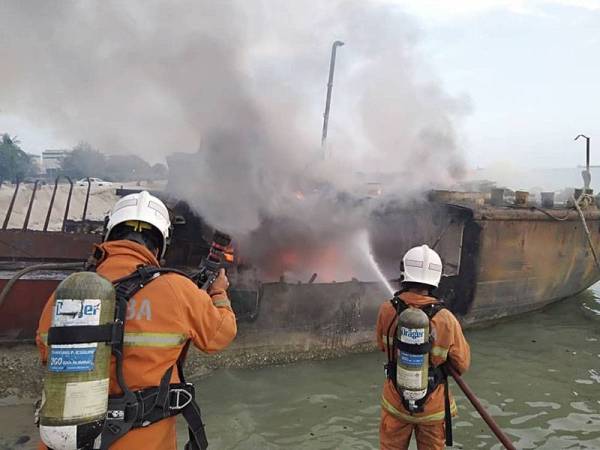 Anggota bomba dan penyelamat sedang melakukan kerja pemadaman kebakaran sebuah kapal korek.