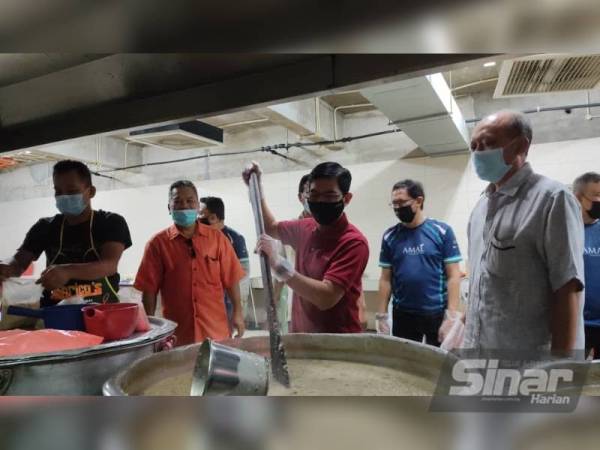 Mohd Muazzam (dua dari kanan) mengacau bubur lambuk sebelum dibungkus untuk diagihkan kepada pasukan barisan hadapan dan pengamal media.