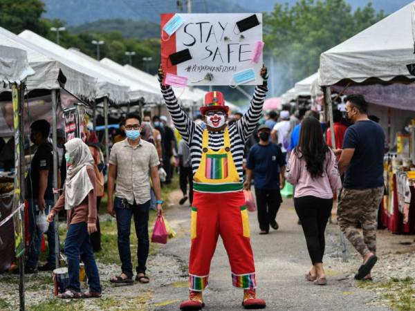 Badut, Mohd Faizal Zainul memegang plakad ‘ Stay Safe’ bagi menyedarkan pengunjung agar mematuhi SOP ekoran kenaikan kes COVID-19 ketika tinjauan di Bazar Ramadhan Taman Jati Meru Ipoh pada Sabtu. - Foto Bernama