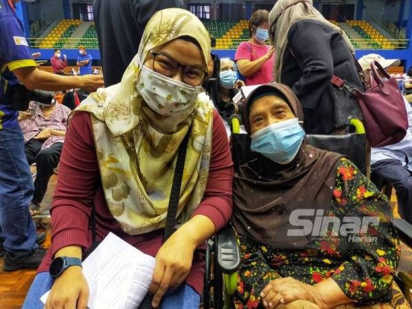 Azizah (kanan) ditemani cucunya hadir menerima suntikan vaksin pada Isnin di Pusat Pemberian Vaksin (PPV) Covid-19 Stadium Tertutup,Sultan Abdul Halim di sini.