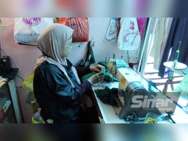 Rofiah tekun menyiapkan tembahan baju pelanggan di kedai jahitnya di Pasar Kuantan pada Isnin.
