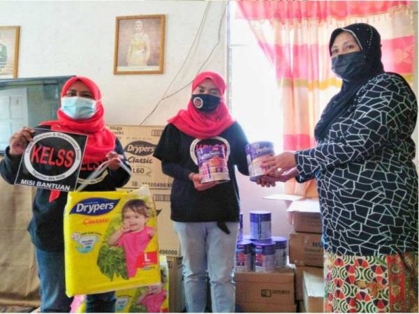 Wakil KELSS menyampaikan sumbangan lampin pakai buang, susu dan beg susu kepada Noor Aini (kanan) ketika berkunjung ke rumah mereka di Kampung Che Dol, Pasir Mas pada Selasa.