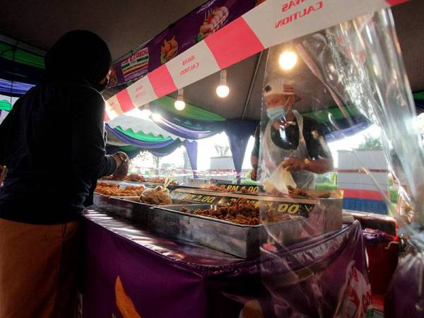 Peniaga melayan pelanggan yang membeli juadah di gerainya dalam suasana norma baharu semasa tinjauan foto Bernama di Bazar Ramadan KotaSAS hari ini. 