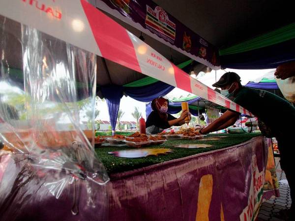 Peniaga melayan pelanggan yang membeli juadah di gerainya dalam suasana norma baharu semasa tinjauan foto Bernama di Bazar Ramadan KotaSAS hari ini. 