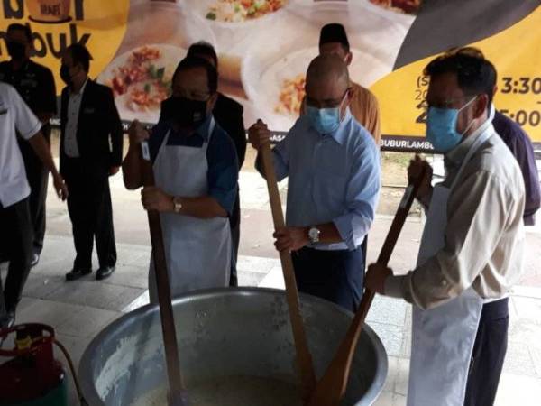 Ahmad (kiri), Ronald (tengah) dan Che Abdullah sedang mengacau bubur lambuk di pekarangan Wisma Tani, Putrajaya pada Selasa.