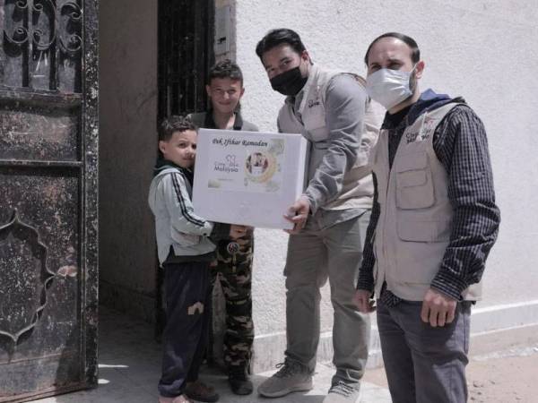 Muhammad Nadir Al-Nuri (tengah) memberikan sumbangan pek iftar Ramadan kepada seorang kanak-kanak di Syria.