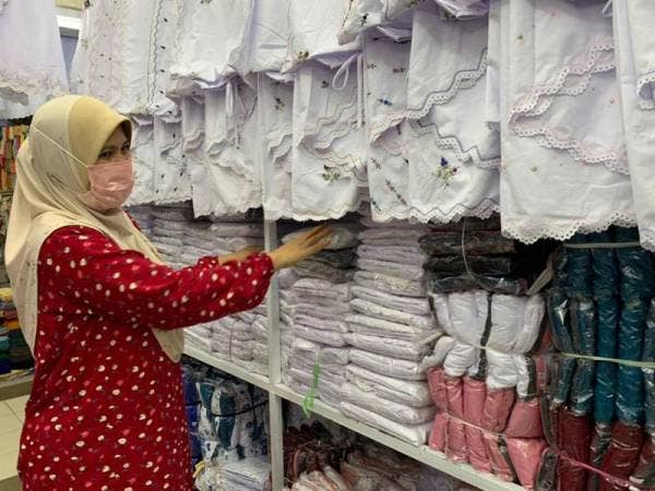 Rosidah Mahmud menyusun kain telekung solat yang dijual di kedainya di sini.