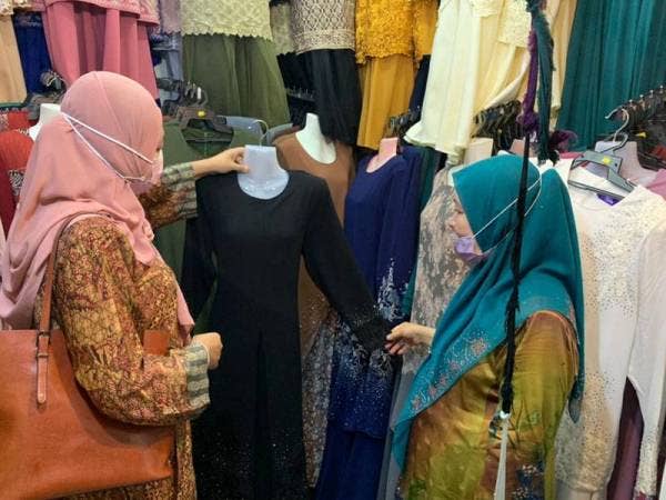 Azizah Omar (kanan) melayani pelanggan di kedainya untuk mencari pakaian.