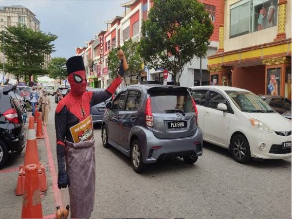 Salah seorang penjual teh ais memakai kostum adiwira cuba menarik pelanggan di kawasan kedai di Seksyen 7, Shah Alam.