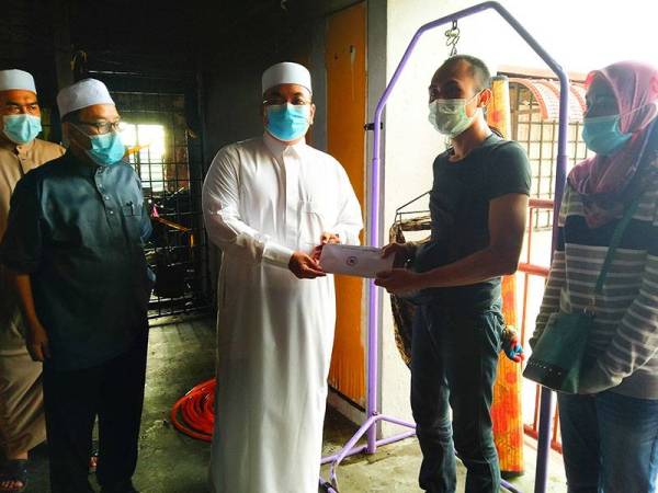 Muhammad Sanusi (tengah) menyampaikan sumbangan kepada Nik Mohd Fairus Nik Man ketika melawat PPR Harmoni Paya Nahu II pada Ahad.