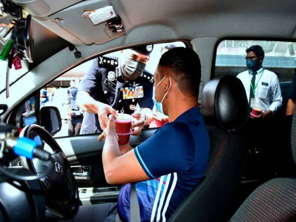 Abdul Majid (kiri) mengagihkan bubur lambuk kepada pengguna jalan raya pada Program Pengedaran Bubur Lambuk kepada Masyarakat Sempena Sambutan Hari Polis ke-214 di Melaka pada Rabu. - Foto Bernama
