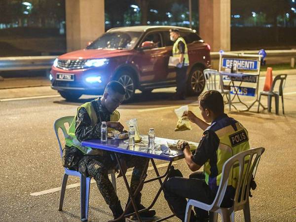 Petugas barisan hadapan keselamatan bergilir menikmati juadah sahur semasa mengadakan sekatan jalan raya di Lebuh Sentosa Presint 7 menghala Lebuhraya Maju Expressway (MEX) awal pagi hari ini.