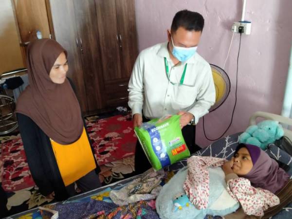 Zamzuri (kanan) menyampaikan sumbangan kepada Aziana yang terlantar sejak lapan tahun lalu akibat dihempap dinding konkrit, di rumah mereka dekat Kampung Bakar Bata, Pinang Tunggal, Sungai Petani pada Ahad.