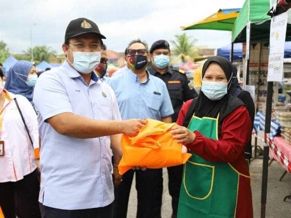 Azhar menyampaikan kit cecair sanitasi tangan berserta pelindung muka dan topi kepada salah seorang peniaga Bazar Ramadan Jalan Meranti, Batang Kali pada Selasa.