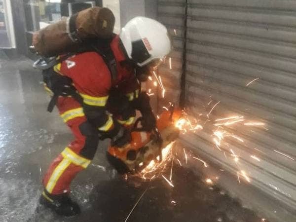 Anggota bomba dan penyelamat memotong pintu 'roller shutter' yang tersekat dengan gergaji khas sebelum kerja-kerja pemadaman dilakukan di sebuah pasar raya di Bandar Meru Raya, Ipoh pada Jumaat.