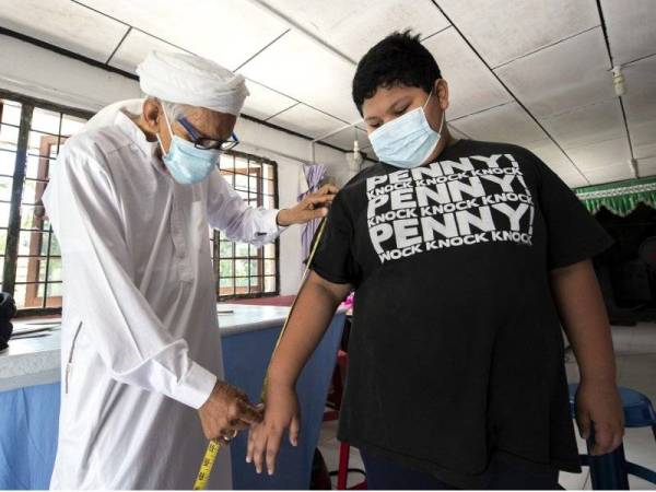 Che Hamat mengambil ukuran baju Melayu Putra Eilman Al-Ziq Afrizam, 12, ketika ditemui di kedai jahitnya Harison Style di Kampung Kubang Cherang, Wakaf Che Yeh. - Foto Bernama