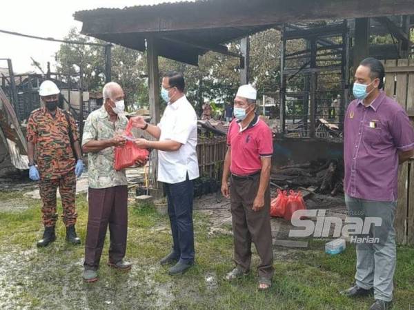 Mohd Azhar (tengah) menyerahkan sumbangan kepada Bahudin di lokasi kejadian kebakaran di Kampung Padang Tembak di sini pada Selasa.