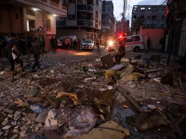 Rakyat Palestin berdiri di atas runtuhan sebuah pangsapuri yang musnah akibat serangan udara Israel di Gaza pada awal hari Selasa. - Foto AFP