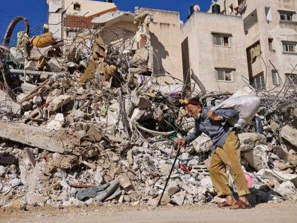 Seorang lelaki Palestin berjalan melintasi serpihan sebuah bangunan yang runtuh akibat serangan bom Tentera Udara Israel baru-baru ini. - Foto AFP