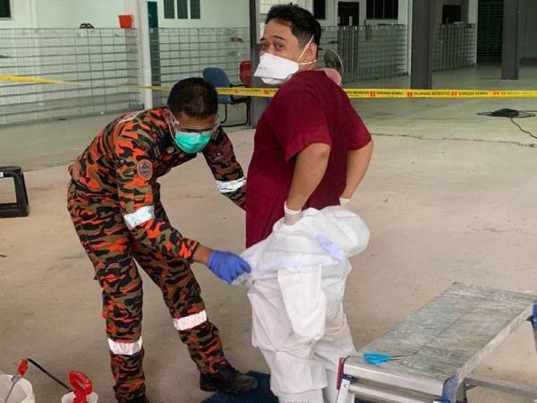 Anggota bomba membantu Zaidi memakai PPE ketika bertugas di Masjid Seri Petaling tahun lalu.