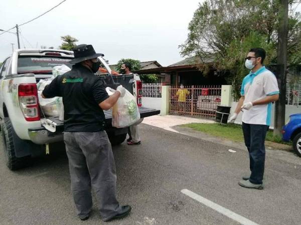 Dr Asmadi (kiri) membawa bungkusan barangan keperluan asas untuk diagihkan kepada penduduk di kawasan yang dikenakan PKPD di Kuantan.