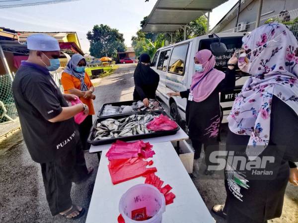 Mohd Zatullah (kiri) melayan penduduk yang mahu membeli ikan.