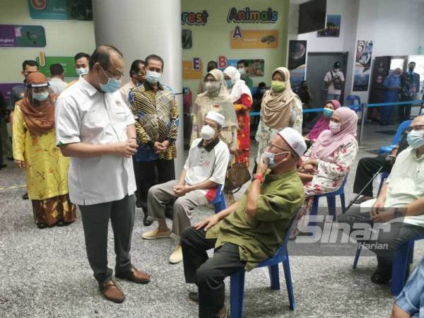 Ahmad Amzad (kiri) berkata sesuatu kepada penerima vaksin yang hadir ke PPV PSKT Kampung Laut pada Khamis.