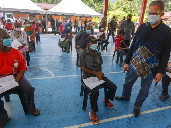 Mustapa (kanan) beramah mesra bersama sebahagian penduduk orang asli yang menunggu giliran untuk menerima suntikan vaksin pada Program Outreach Vaksinasi Covid-19 di Kampung Sungai Rual, Jeli pada Sabtu. - Foto Bernama