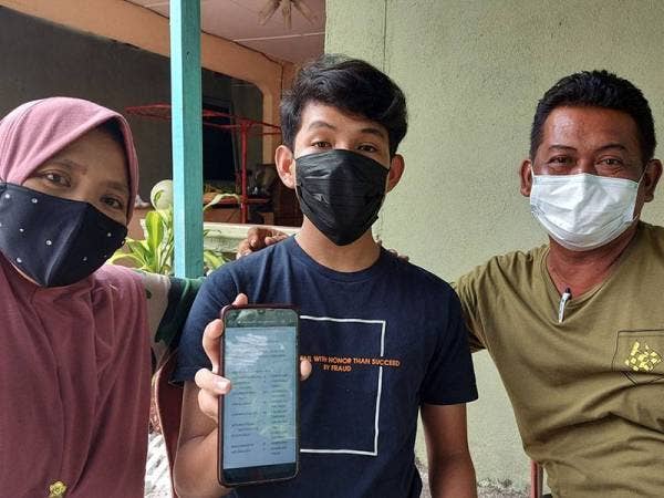Aiman Aqil (tengah) ditemani ibu bapanya menunjukkan keputusan SPM yang diperolehnya di Kampung Sadang, Parit pada Khamis.