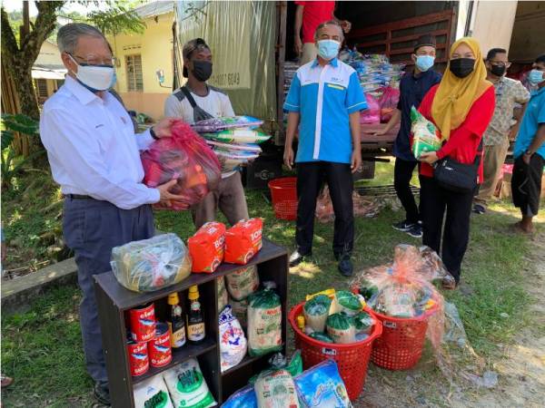 Mustapa (kiri) menyampaikan sumbangan bakul makanan yang disediakan kepada penduduk orang asli yang menerima vaksin pada Program Outreach Covid-19 di Dewan Serbaguna Kampung Sungai Rual, Jeli pada Sabtu.