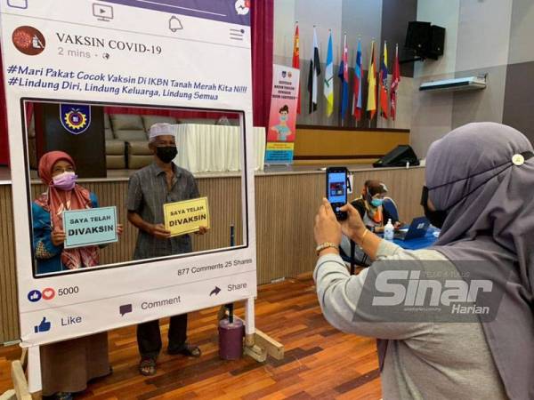 Che Rohayah mengambil gambar kedua-dua ibu bapanya selepas selesai menerima vaksin masing-masing.