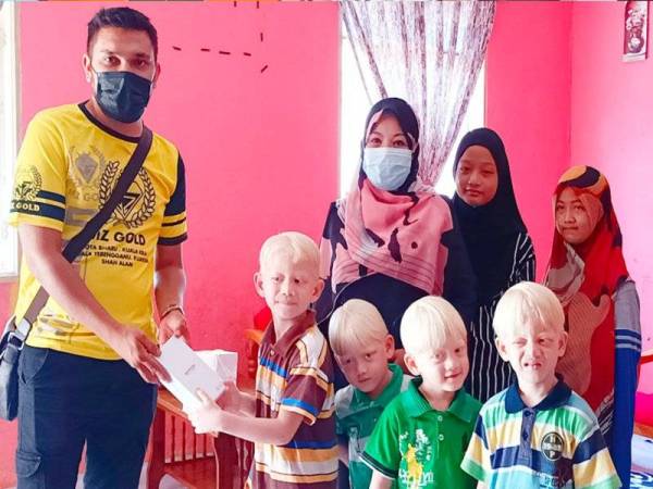 Murtadhatumizi (kiri) daripada MZ Gold menyampaikan sumbangan telefon pintar untuk kegunaan PdPR kepada Muhammad Adam Haris (empat dari kanan) yang merupakan murid darjah satu.