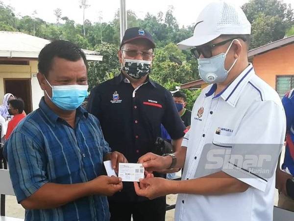 Maximus menyerahkan kad vaksinasi Covid-19 kepada salah seorang penduduk selepas selesai menerima dos pertama pada Program Vaksinasi di Kampung Sungai Magandai pada Selasa.