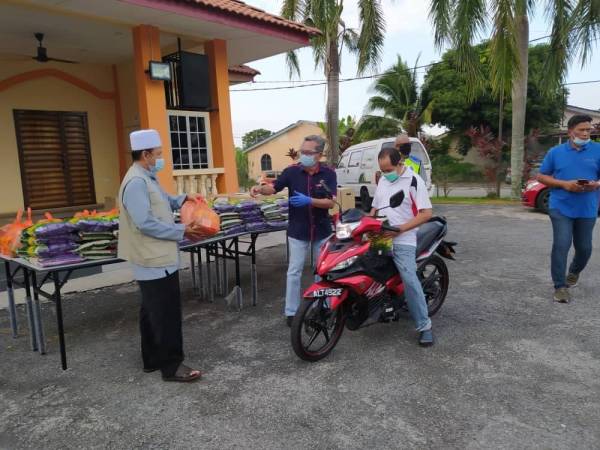 Azizul Kama (dua dari kiri) menyerahkan sumbangan kepada peniaga yang terjejas pada Program Kongsi Rezeki secara pandu lalu di perkarangan Masjid Jamek Medan Klebang Restu, di sini pada Ahad. 